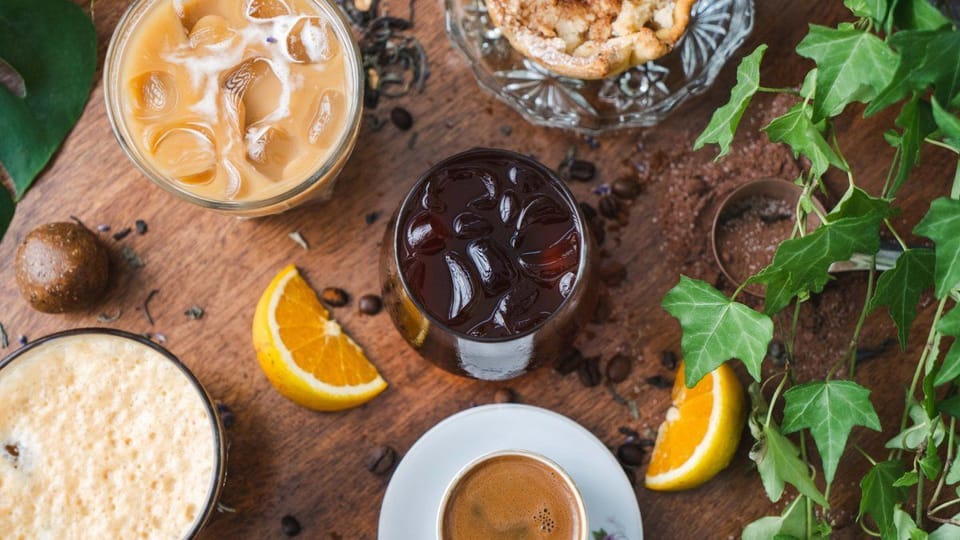 Iced latte, cold brew, freddo and a Cypriot coffee on a wooden table with orange slices, coffee beans and an apple crumble tart.