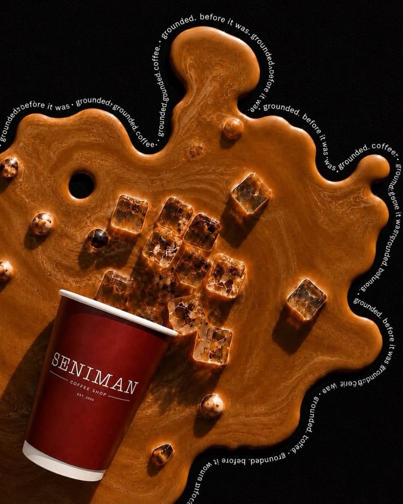 A burgundy Seniman takeaway cup tipped over on black, coffee and ice cubes spilling out in a glossy caramel pool.